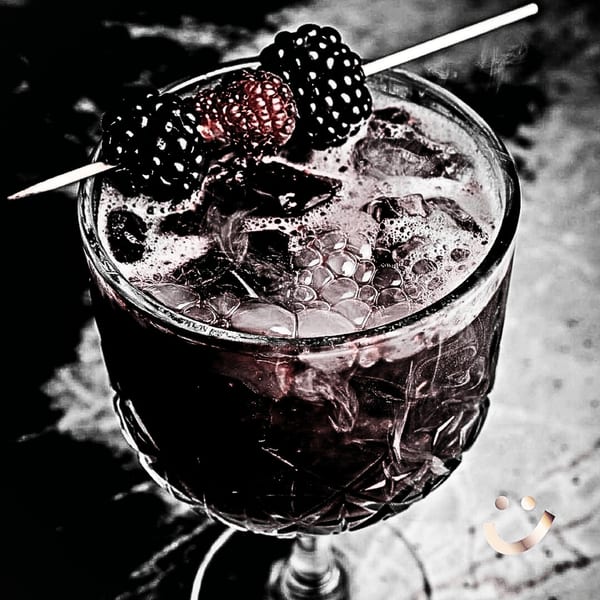A dark La Buena Vida cocktail with ice, garnished with blackberries and raspberries on a skewer.