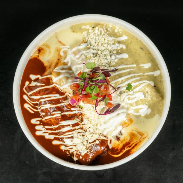 A white bowl filled with enchiladas covered in red, green, and white sauces, topped with cheese and pico de gallo.