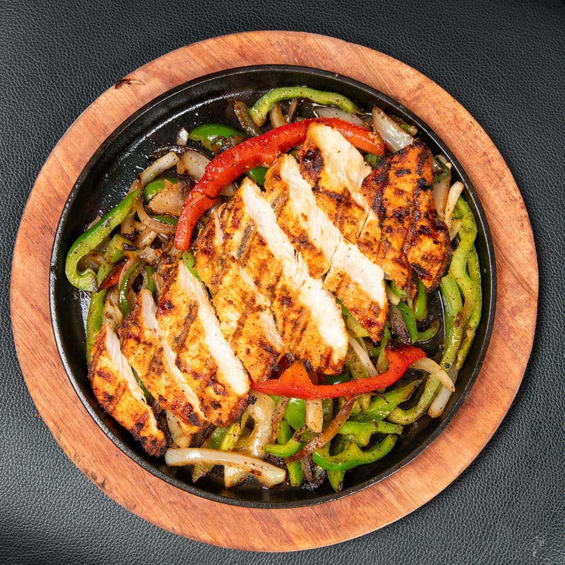 Sizzling chicken fajitas with grilled onions, red and green bell peppers on a cast iron skillet.