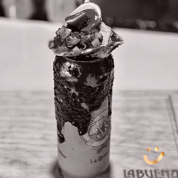 Black and white image of a michelada topped with an oyster, pico de gallo, and a lime.