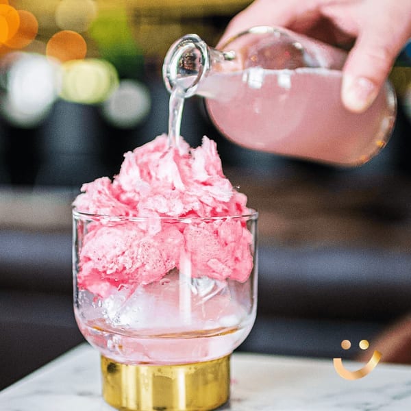 Pink liquid being poured from a bottle into a glass with pink cotton candy and ice.