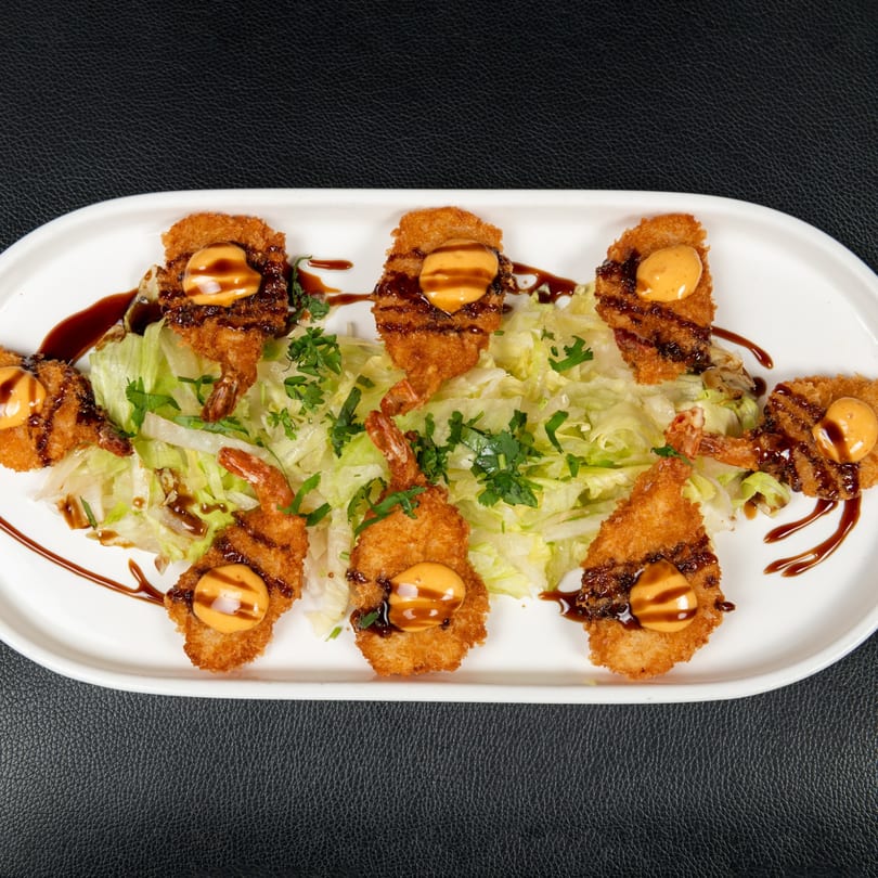 Crispy fried shrimp with orange sauce and dark drizzle, served on a bed of lettuce.