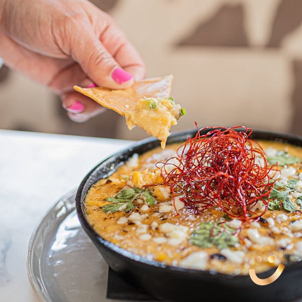 Hand with pink nails dipping a tortilla chip into a skillet of La Buena Vida's Mexican queso.