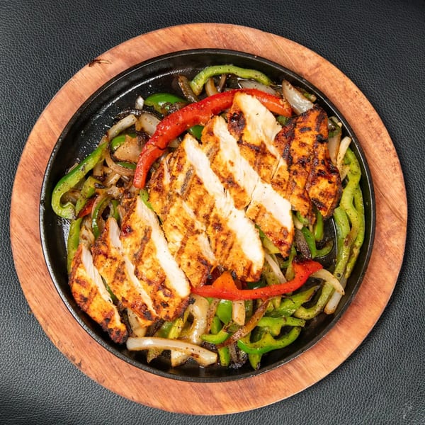 Sizzling chicken fajitas with grilled onions, red and green bell peppers on a cast iron skillet.