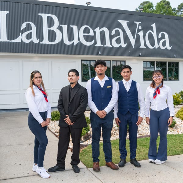 Five La Buena Vida restaurant staff members in uniform stand outside the building entrance.