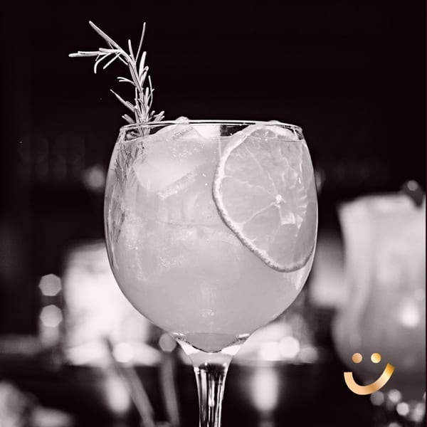 Black and white close-up of a cocktail with a citrus slice and rosemary sprig.