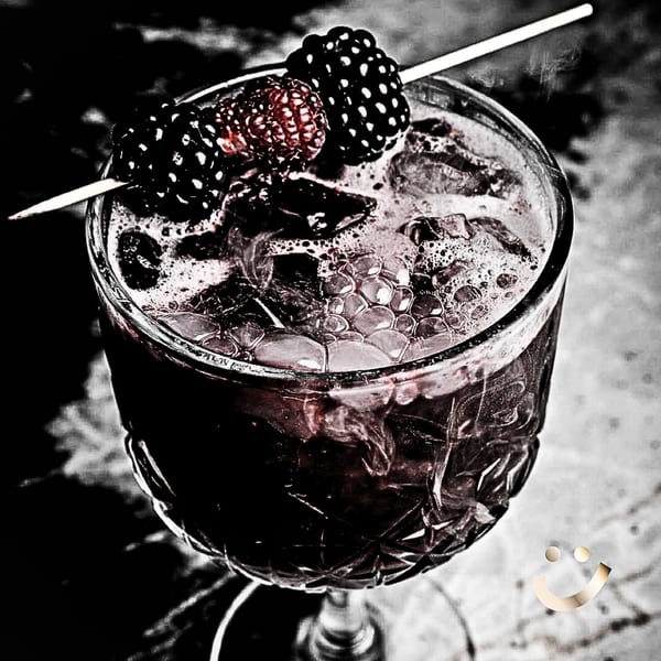 Dark berry cocktail with ice and a skewer of blackberries and raspberries in a cut glass.