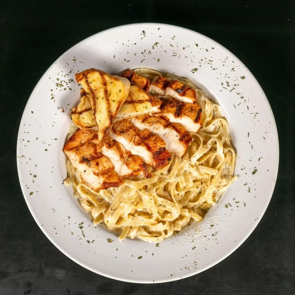 Grilled chicken and garlic bread served over creamy fettuccine alfredo, garnished with herbs.
