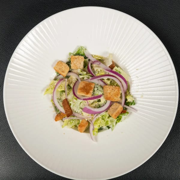 Caesar salad with romaine lettuce, red onion, croutons, and parmesan cheese on a white plate.