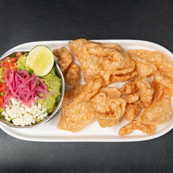 Guacamole with pickled red onions, crumbled cheese, and a lime wedge, served with chicharrones.