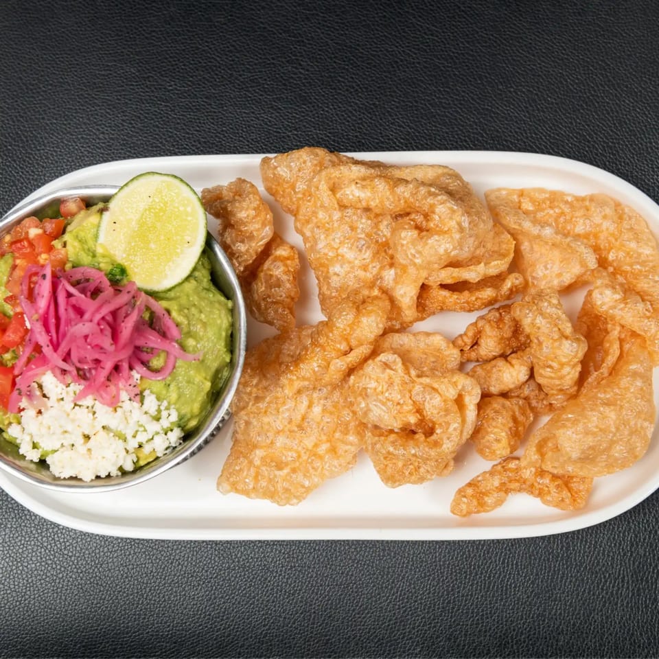 Guacamole with pickled red onions, crumbled cheese, and a lime wedge, served with chicharrones.