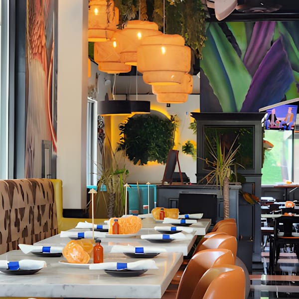A vibrant La Buena Vida dining room with set tables, orange chairs, and tropical decor.