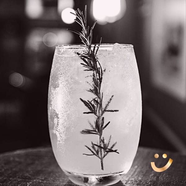 Black and white close-up of a La Buena Vida cocktail with rosemary garnish and ice.