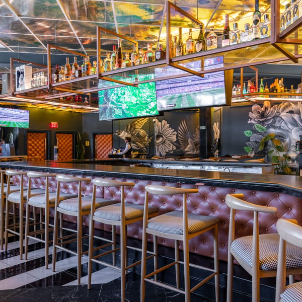 A modern bar with liquor bottles, multiple TVs, and a bartender behind the counter.