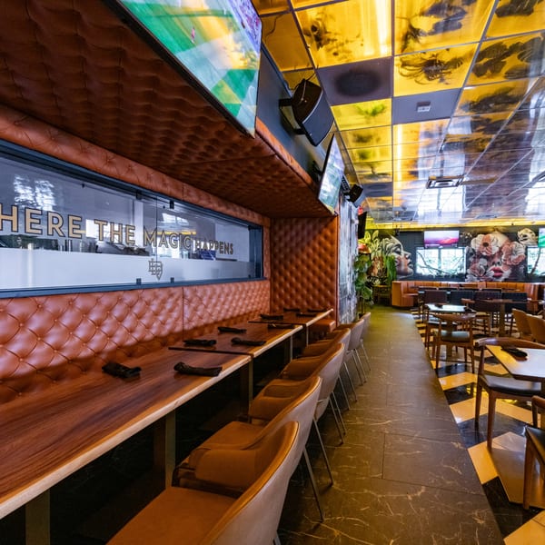 A restaurant interior with tufted brown leather booths, wooden tables, and a black and yellow patterned ceiling.
