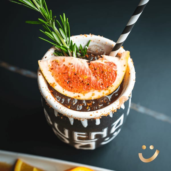 A La Buena Vida cocktail in a black and white mug, garnished with grapefruit and rosemary.